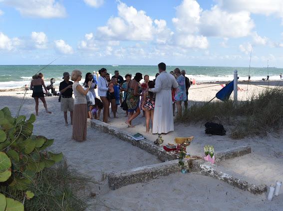 Priest blessing a visitor beside the Miracle Cross on the sand